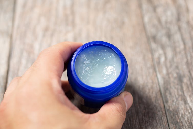 Hand holding small container of topical ointment